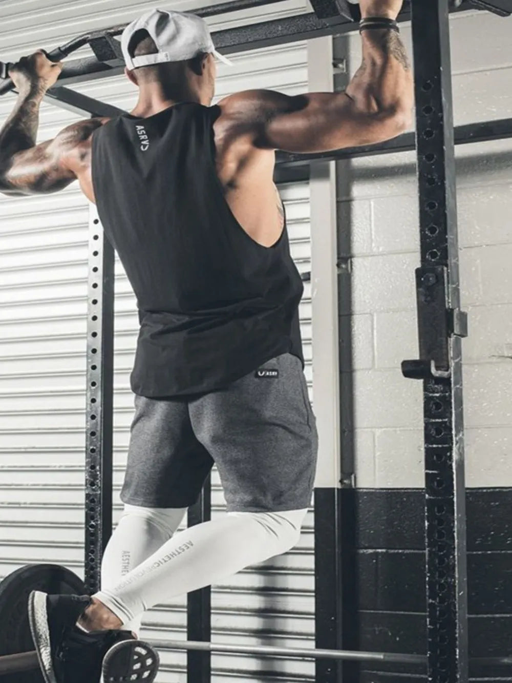 Black scoop neck muscle tank top with a relaxed fit, worn by a man doing pull-ups.