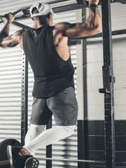 Black scoop neck muscle tank top with a relaxed fit, worn by a man doing pull-ups.