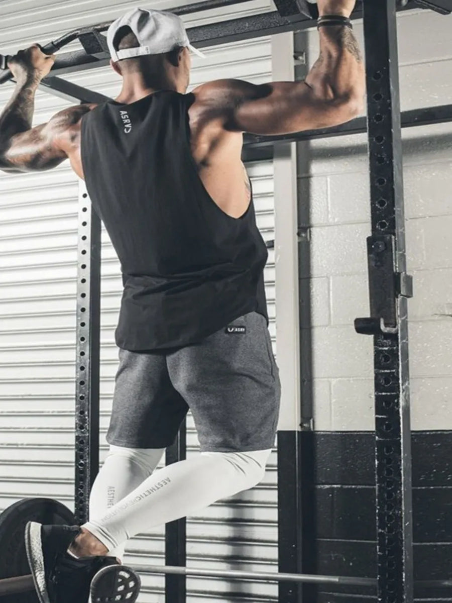 Black scoop neck muscle tank top with a relaxed fit, worn by a man doing pull-ups.