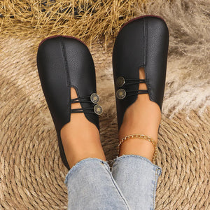 Black leather slip-on flats with button detail and elastic straps.