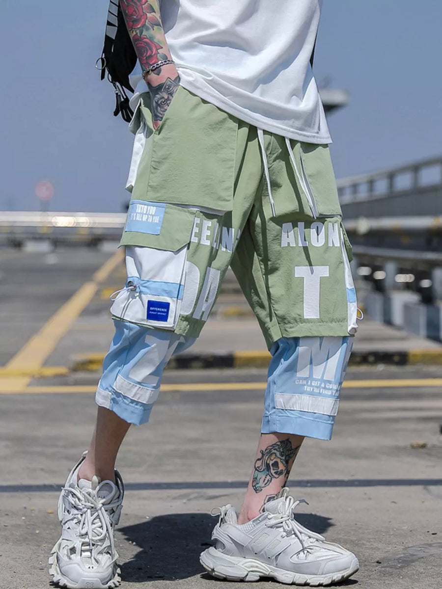 Color block utility cargo pants in light green and light blue with bold white text graphics and multiple pockets.