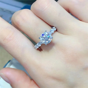 Silver moissanite halo ring with pavé band and round center stone.