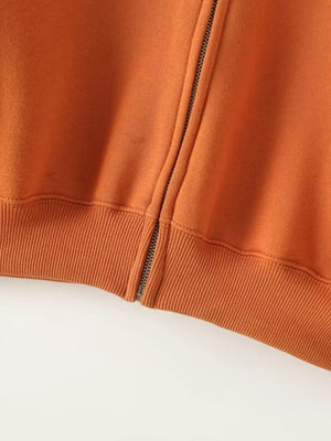 Orange zip-up top with ribbed hem detail and side zipper accent.
