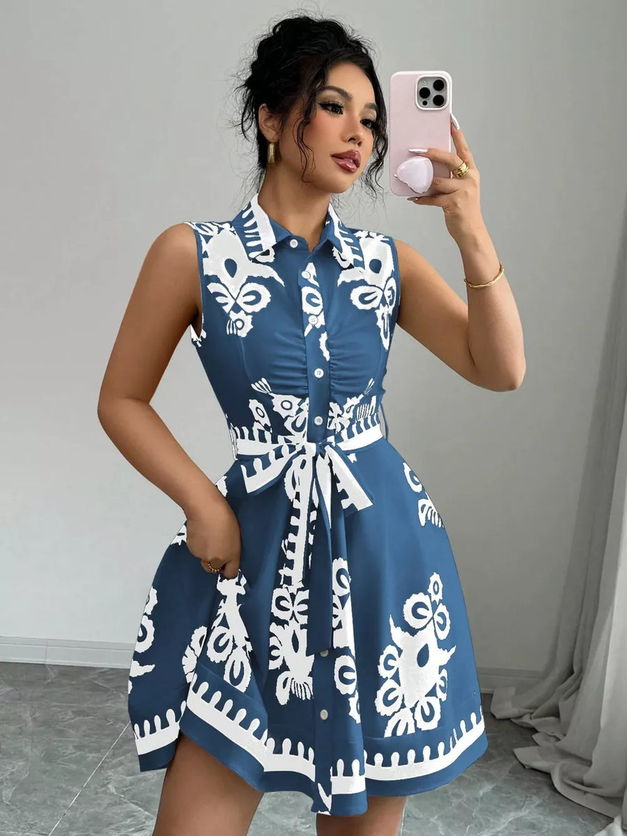 Dusty blue sleeveless button-down shirt dress with white abstract print and tie waist.