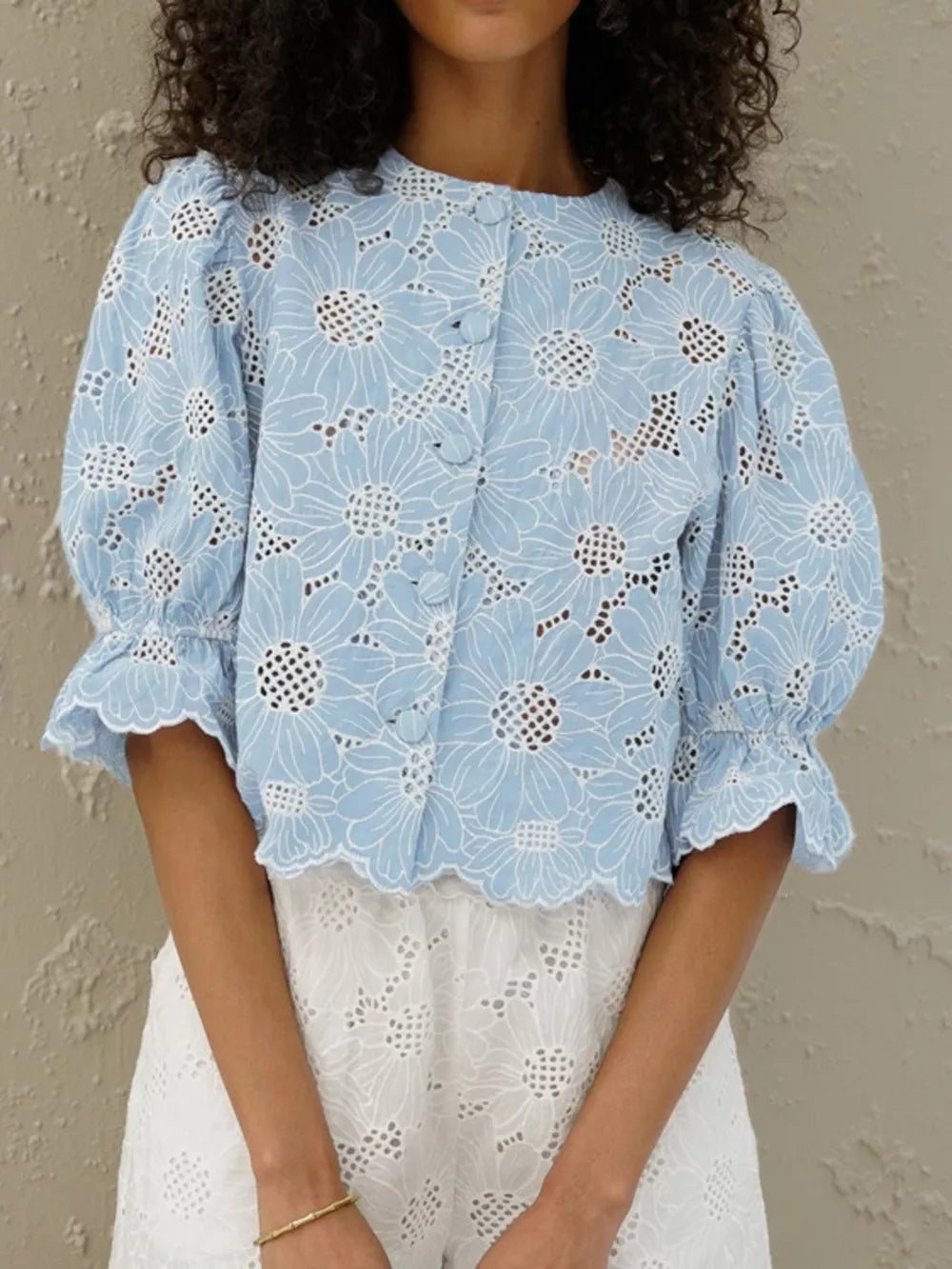 Blue eyelet crop top with white floral embroidery, puff sleeves, and ruffled cuffs.