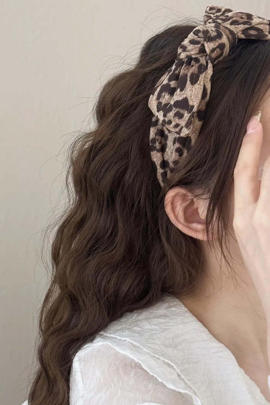 Leopard print knotted headband with a bow detail, worn by a woman with wavy brown hair.