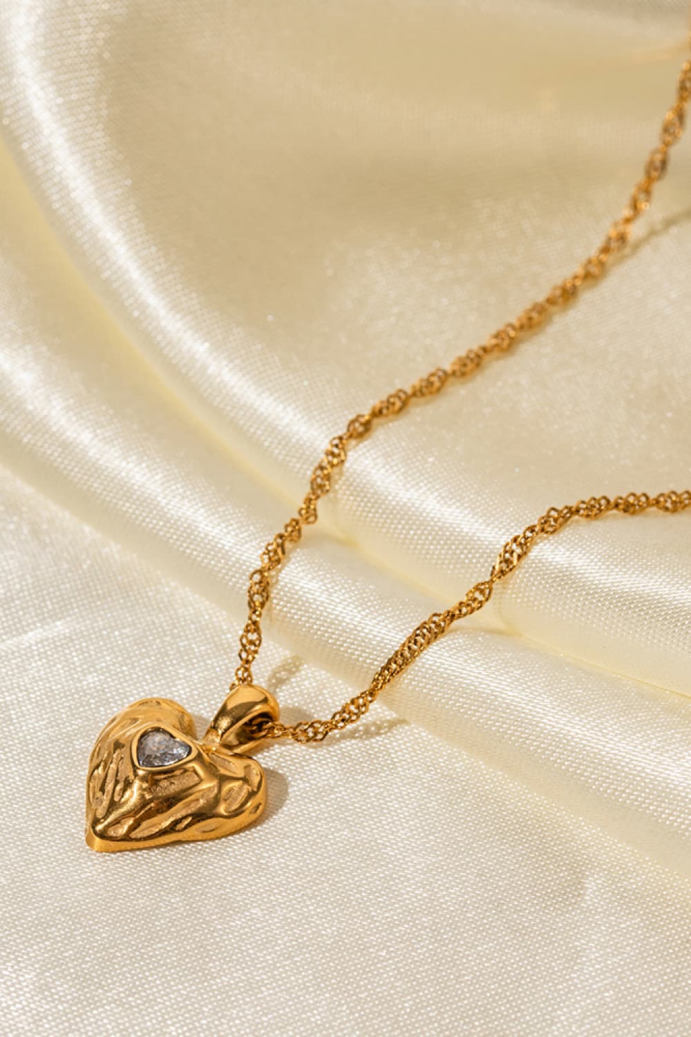 Textured gold heart pendant necklace with a small clear stone on a delicate chain.