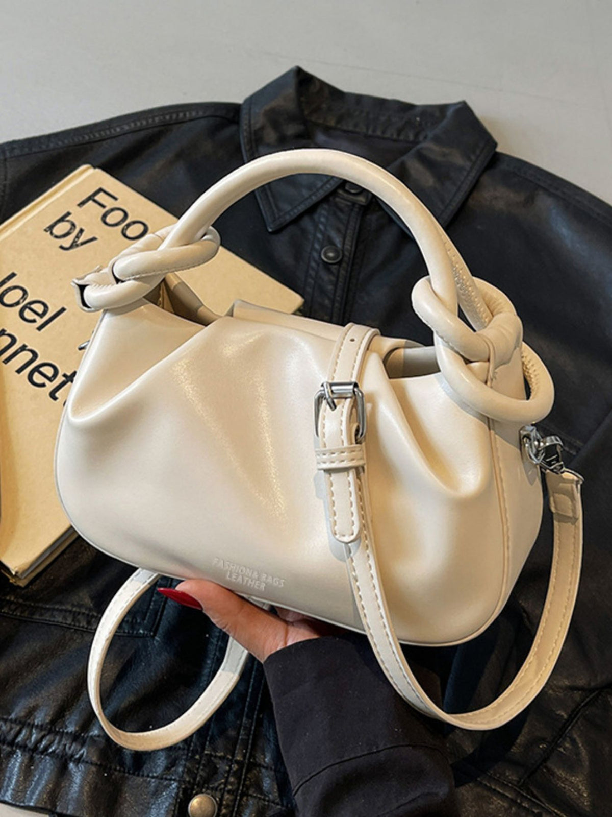 Off-white ruched crossbody bag with knot handle and adjustable strap.