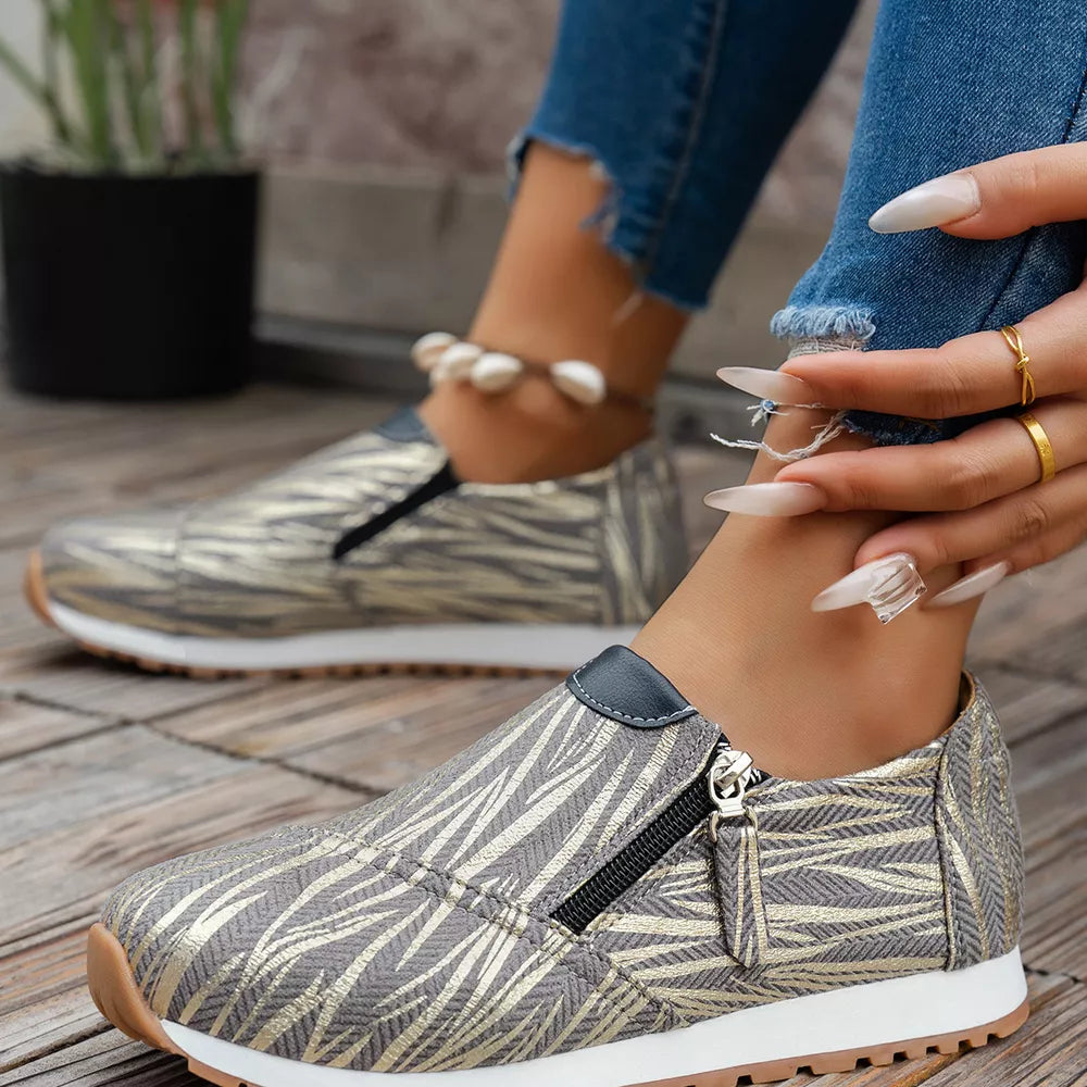 Zebra print slip-on flats in grey with gold accents and side zipper detail.