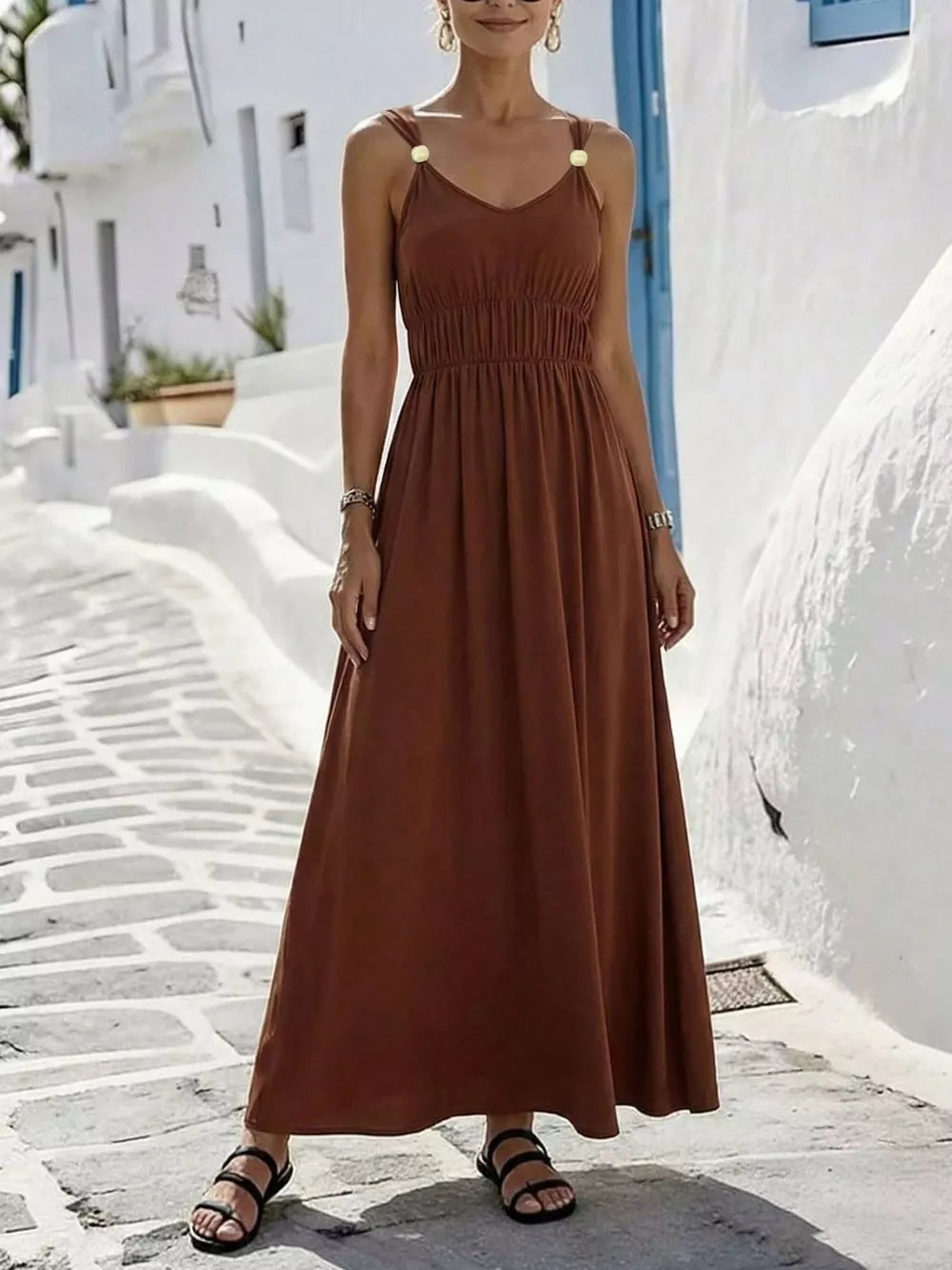 Brown V-neck sleeveless maxi dress with smocked waist and gold-tone shoulder details.