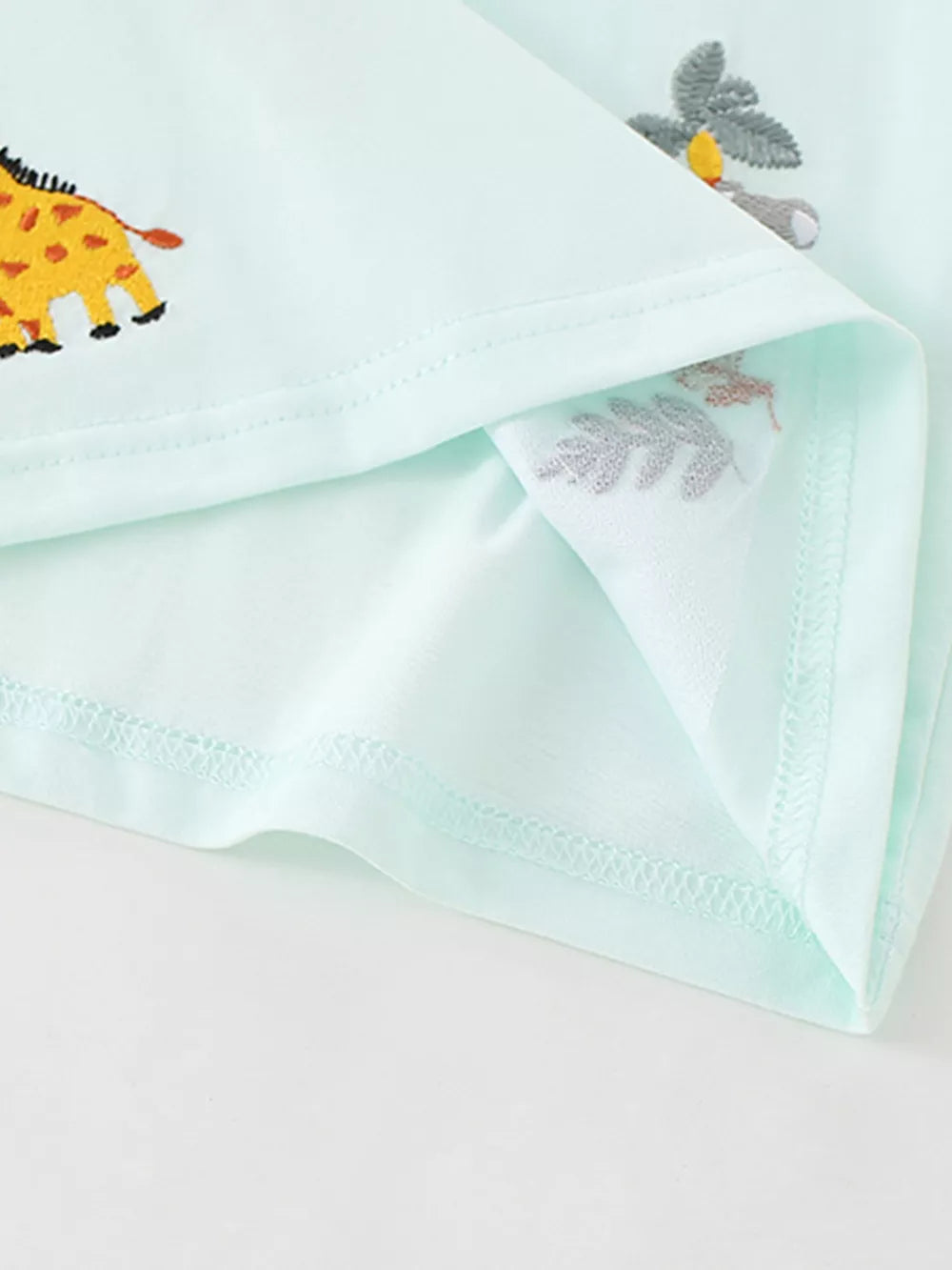 Light blue baby polo shirt with embroidered giraffe and botanical details.