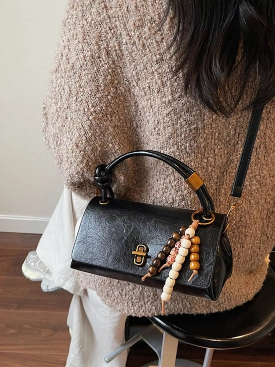 Black leather crossbody bag with beaded charm detail and turn-lock closure