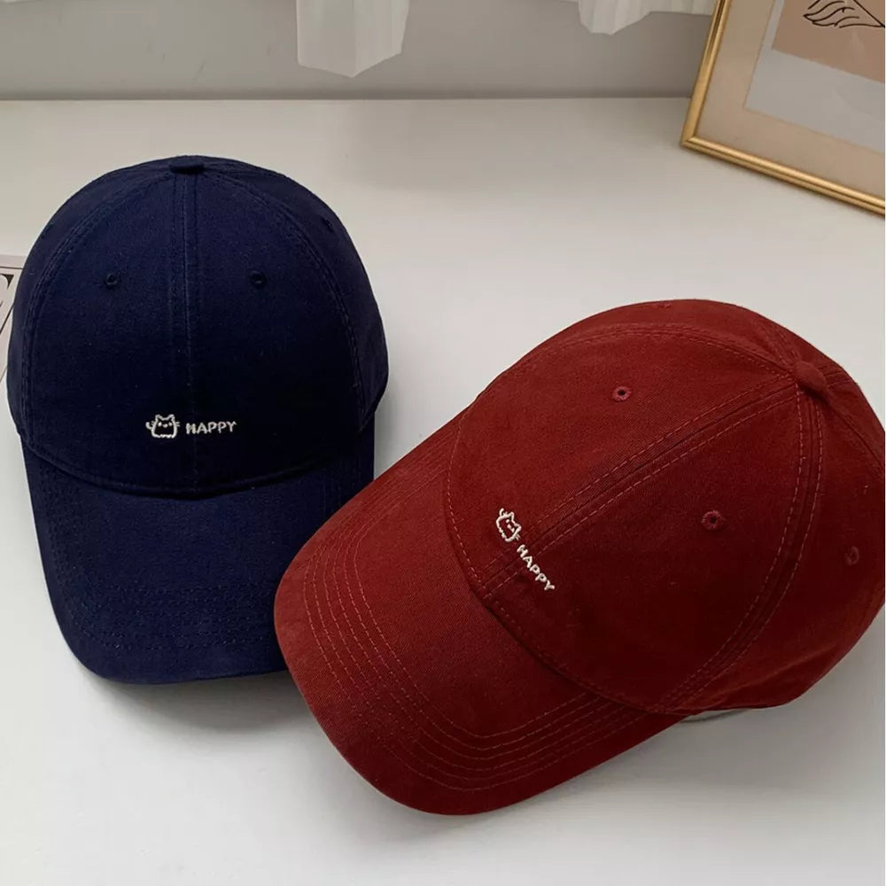Navy and wine red cotton baseball hats with embroidered cat and HAPPY detail.