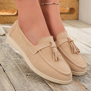 Beige faux-suede slip-on loafers with decorative tassels and contrast stitching.