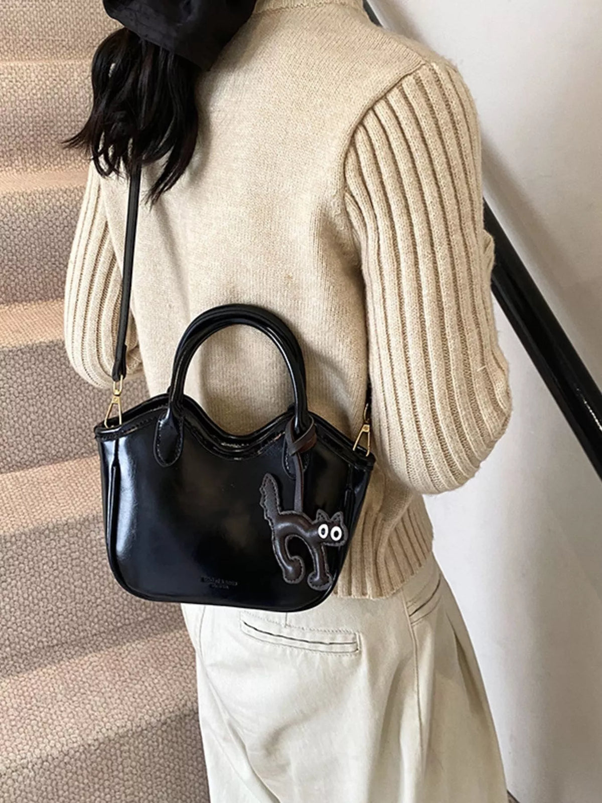 Black patent leather crossbody bag with a cute cat charm and top handles.