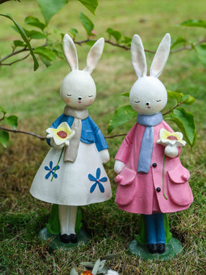 Floral resin rabbit figurines in blue and pink coats, holding flowers.