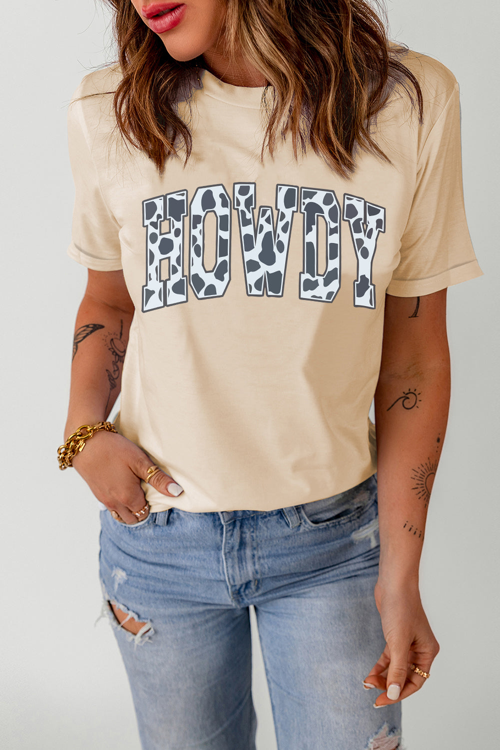 Light apricot graphic tee with cow print "Howdy" text, crew neck, short sleeves.