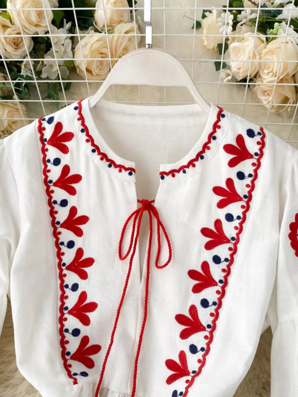 White maxi dress with red and blue floral embroidery and tie neck.