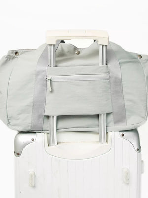 Light gray athletic nylon tote with zippered pocket and trolley sleeve, shown on a suitcase.
