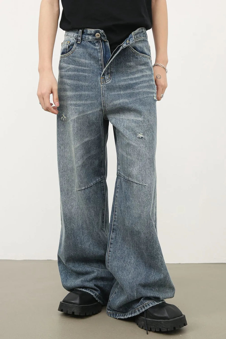 Distressed edge wide-leg denim jeans in medium wash with ripped details and patchwork.
