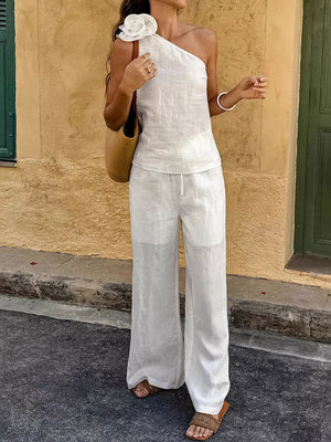 White cotton one-shoulder top with floral embellishment and wide-leg pants.