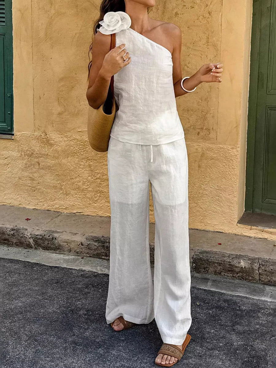 White cotton one-shoulder top with floral embellishment and wide-leg pants.