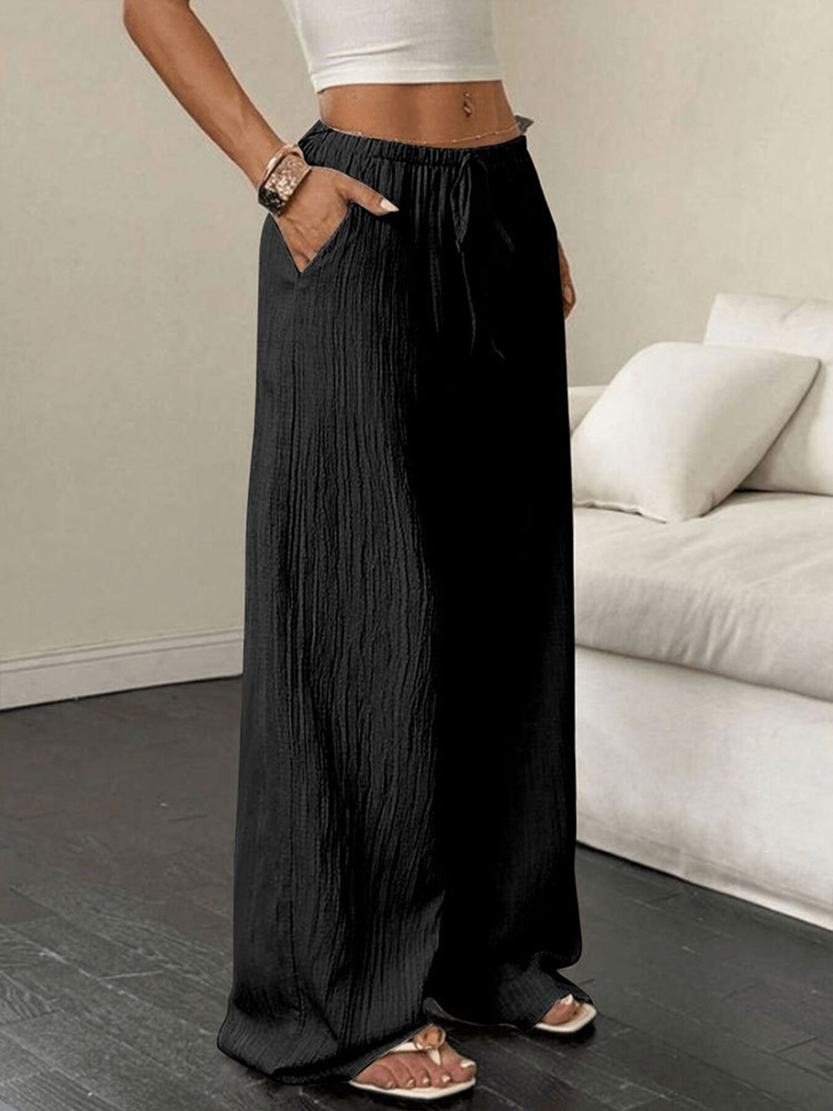 Black crinkled wide-leg drawstring pants with pockets, styled casually.