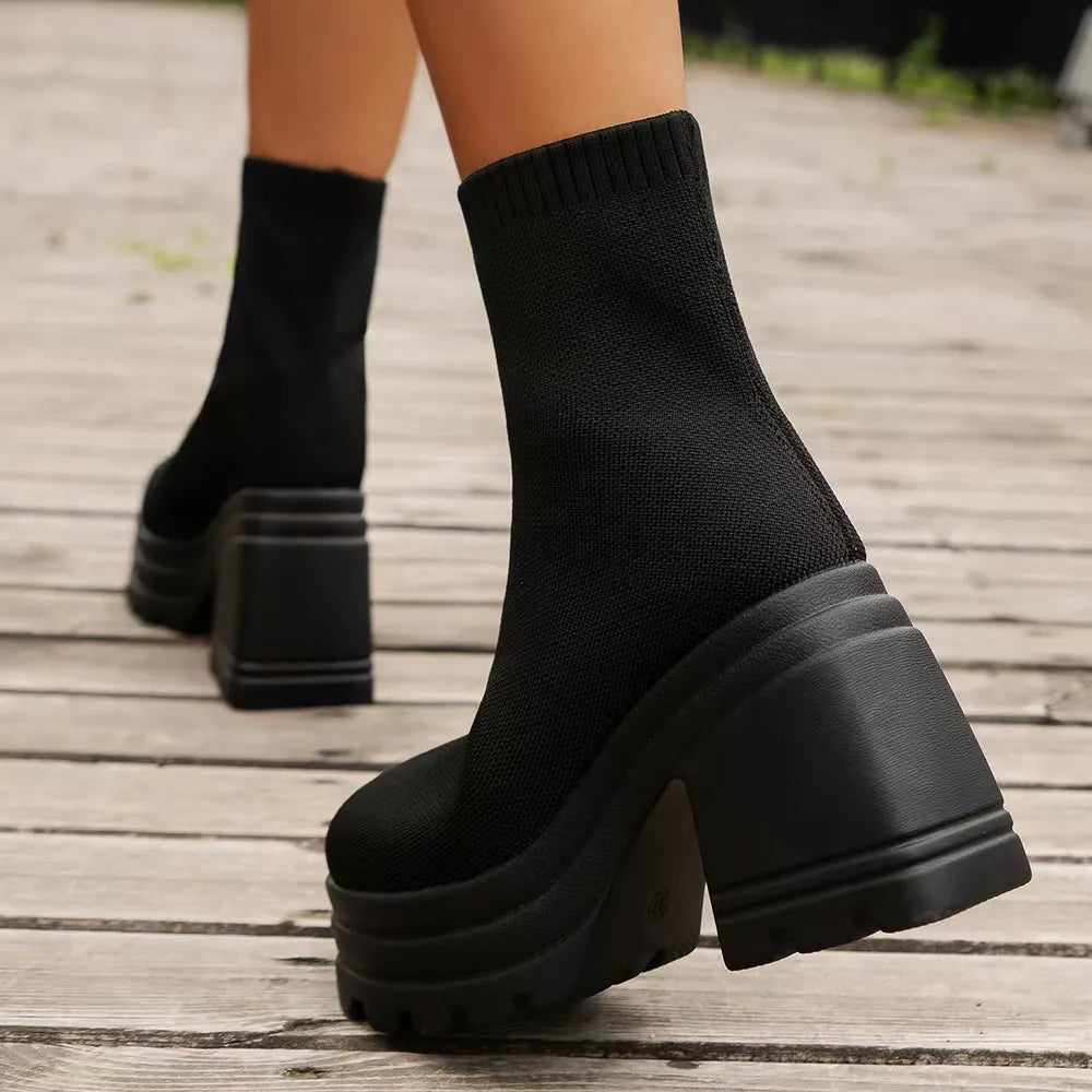 Black knit sock boots with chunky platform and heel on wooden planks.