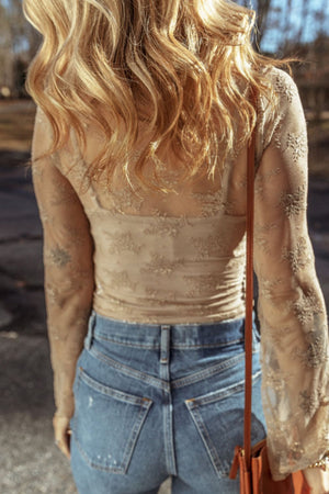 Tan floral lace bodysuit with long sleeves and a square neckline, styled with denim jeans.