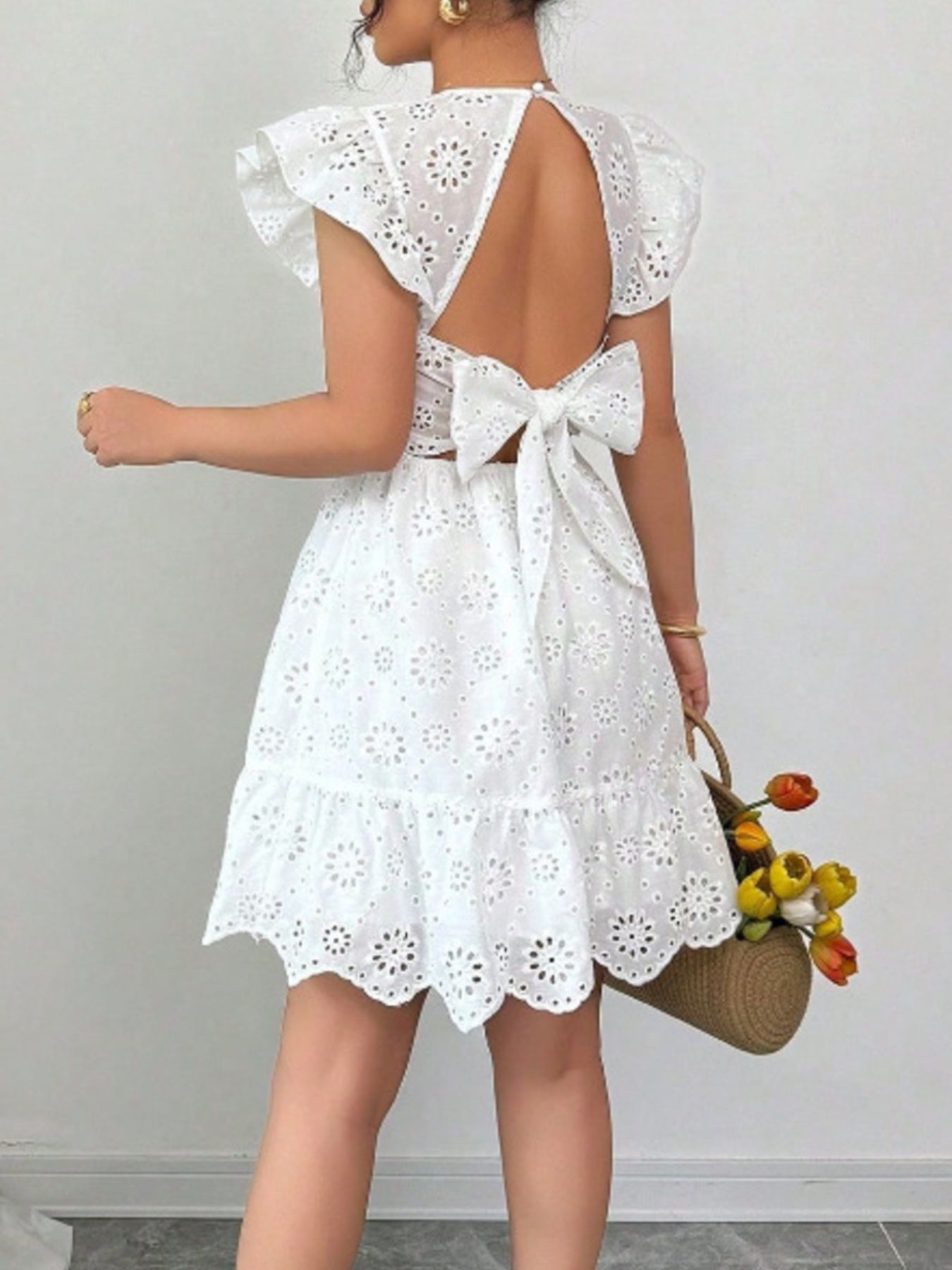 White eyelet mini dress with ruffle sleeves, backless design, and large bow detail.