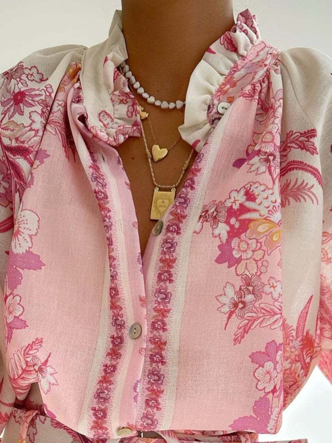 Pink floral print button-up shirt with ruffled collar and button details.