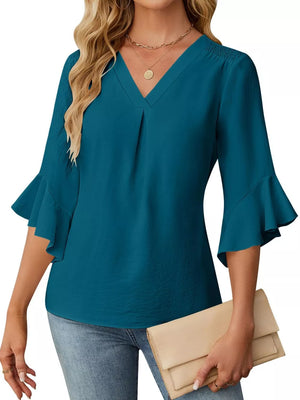 Teal V-neck blouse with ruffle sleeves and smocked shoulders, paired with jeans and a clutch.