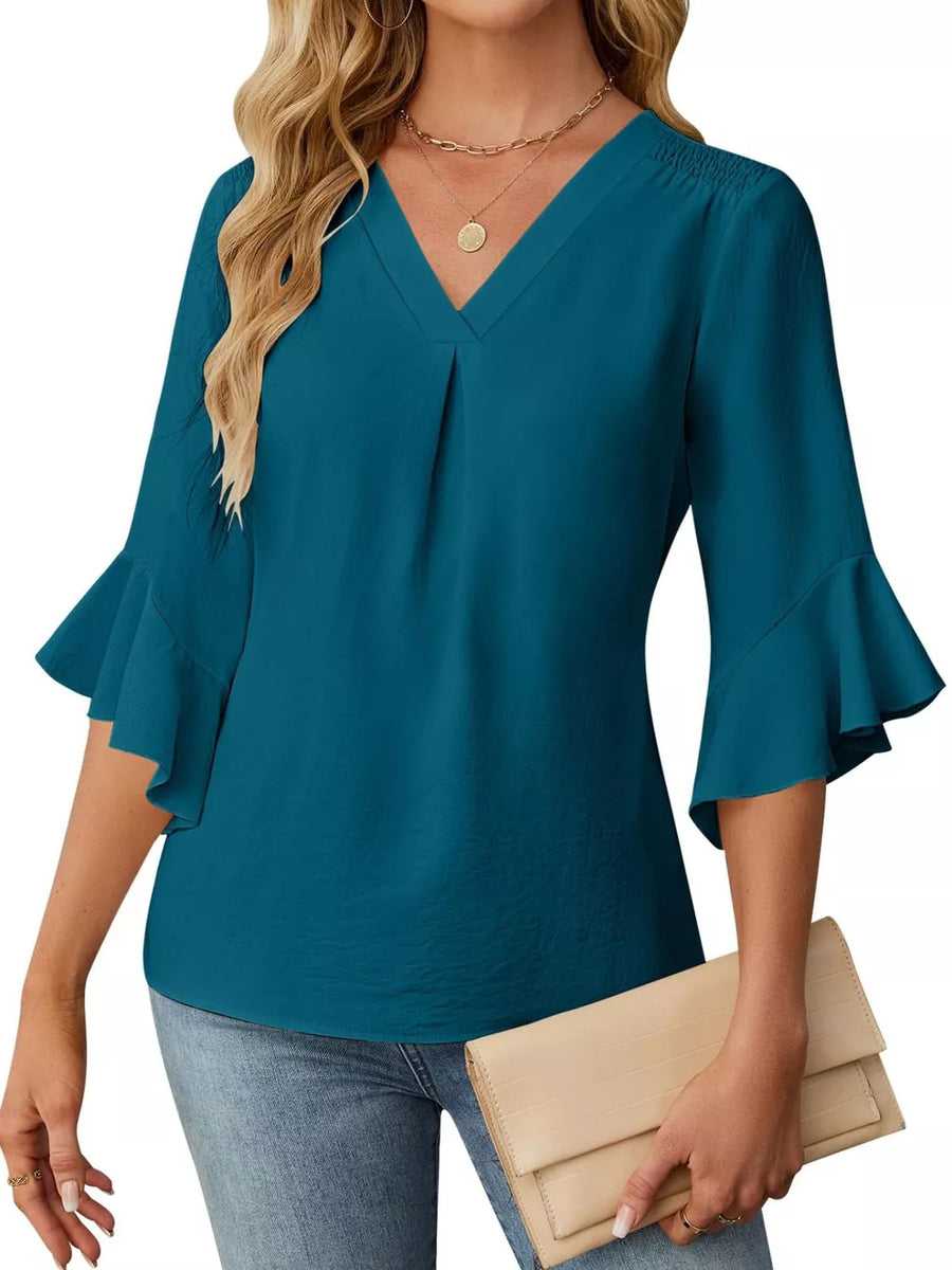 Teal V-neck blouse with ruffle sleeves and smocked shoulders, paired with jeans and a clutch.