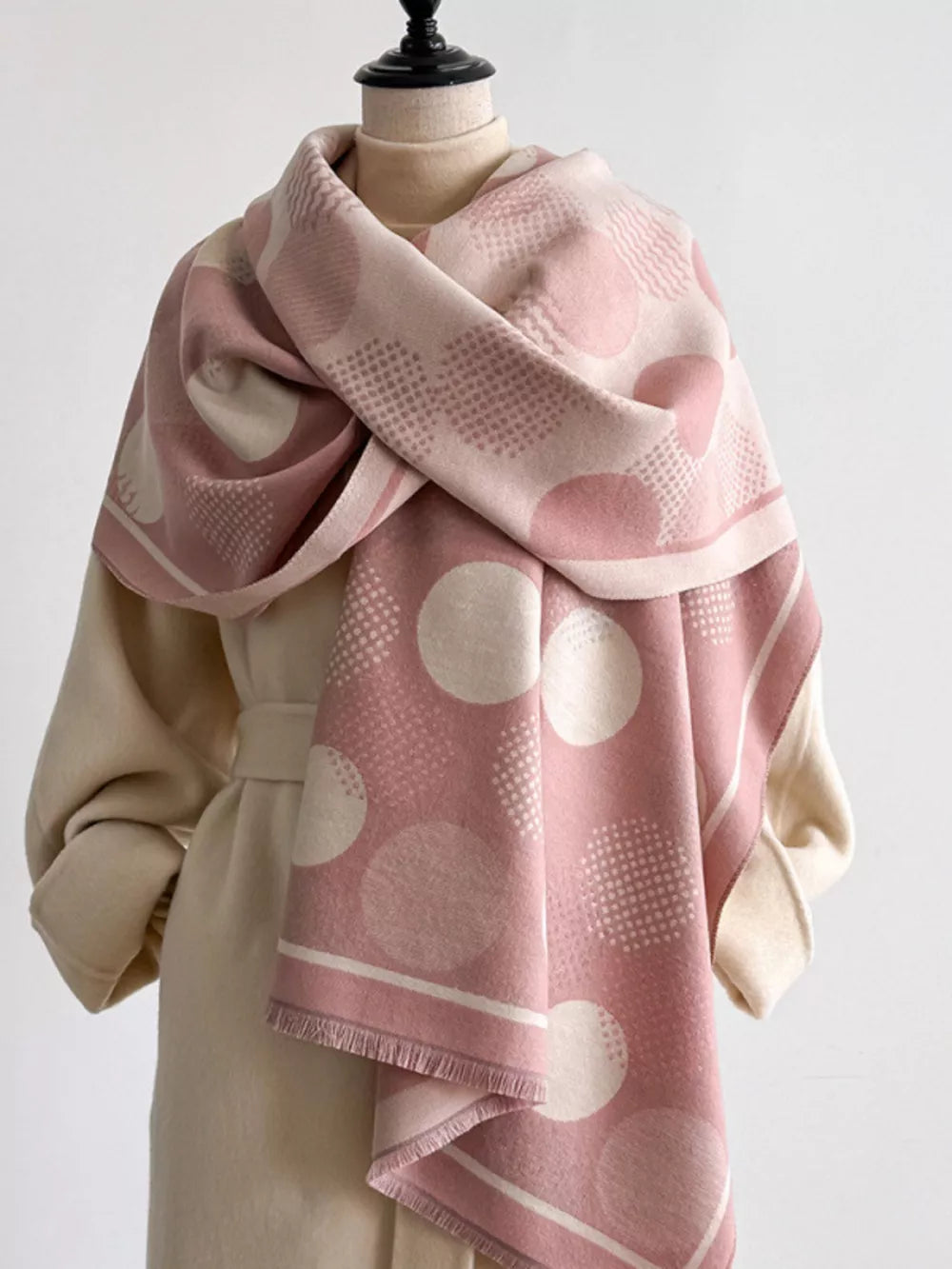 Dusty pink textured scarf with large polka dots and a fringe hem, styled with a beige coat.