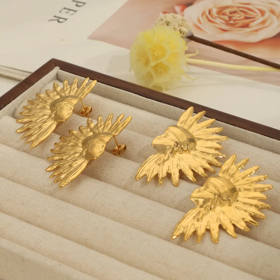 Gold sculptural face earrings with sunburst detail.
