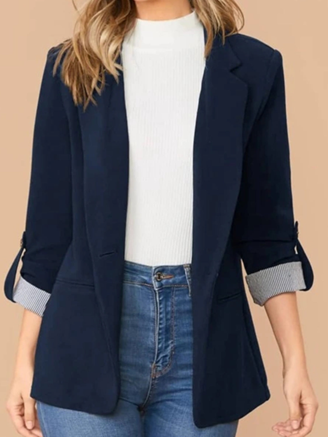 Dark blue cuffed sleeve tailored blazer with striped cuffs, worn open over a white top and jeans.