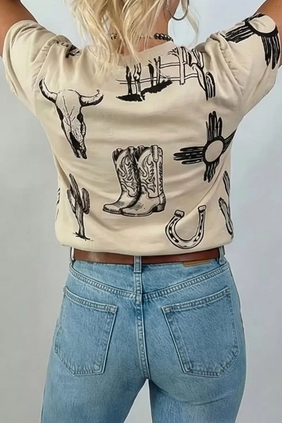 Cream crew neck t-shirt with western graphic print including bull skull, boots, cactus, horseshoe and sun symbol.