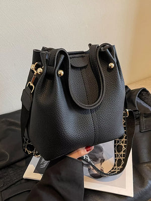 Black textured crossbody bag with unique patterned strap and gold hardware.
