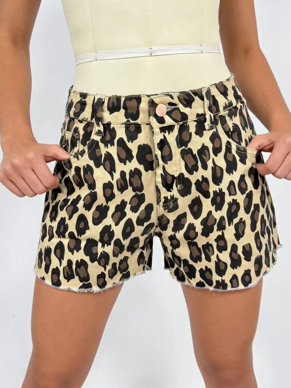 Leopard print high-waisted denim shorts with raw hem and button fly.