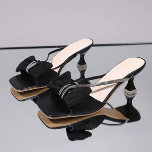 Black heeled mules with crystal bow detail and clear heel accents.