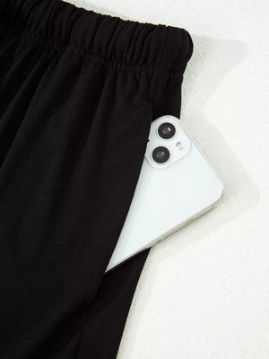Black pajama pants with elastic waist and side pocket holding a smartphone.