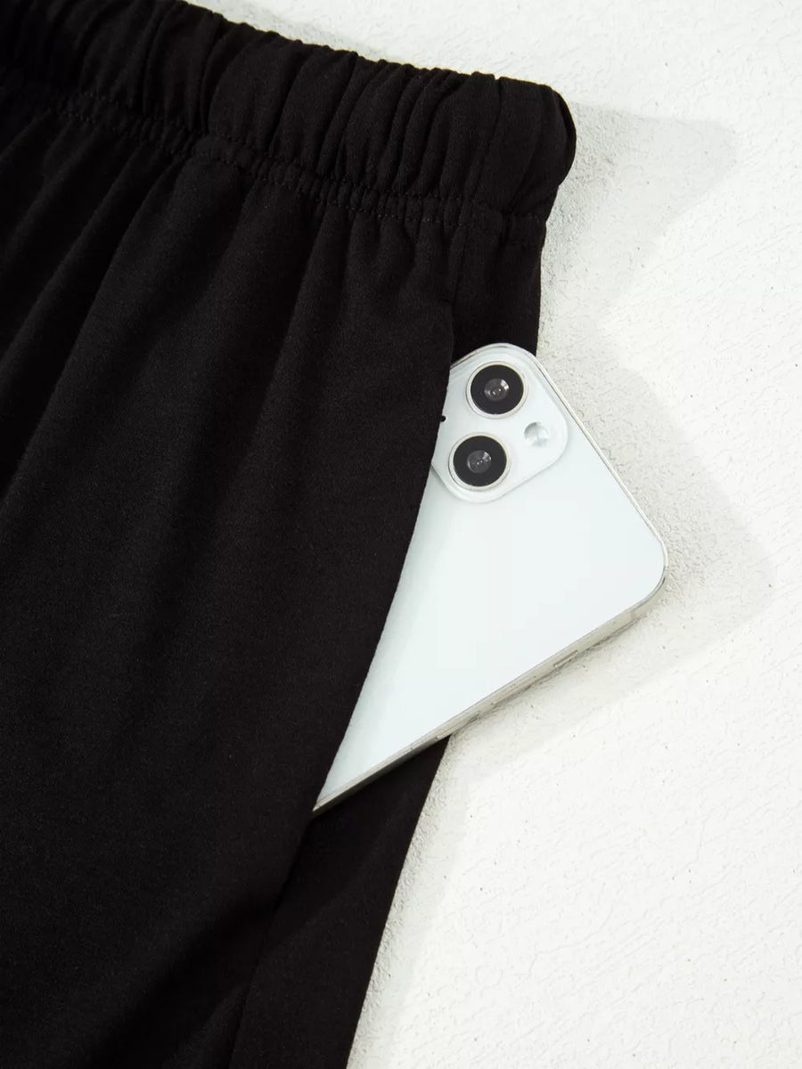 Black pajama pants with elastic waist and side pocket holding a smartphone.