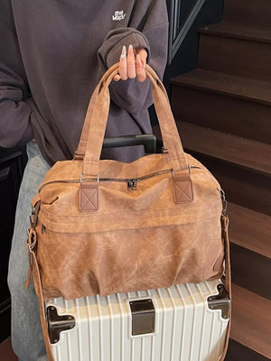Brown suede duffel bag with dual handles and a crossbody strap, styled with a grey sweatshirt.