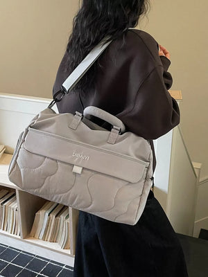Quilted grey duffel bag with adjustable strap and top handles, featuring a front flap pocket.