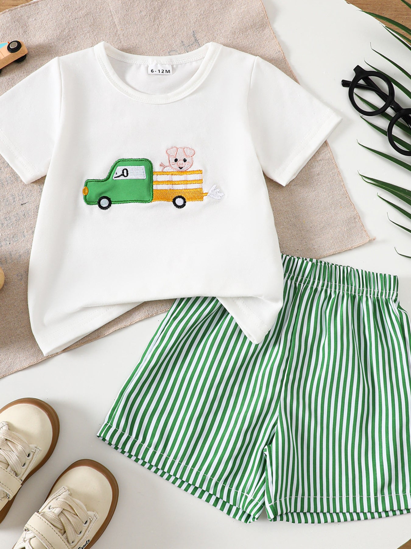 White baby tee with embroidered tractor and pig, green striped shorts.