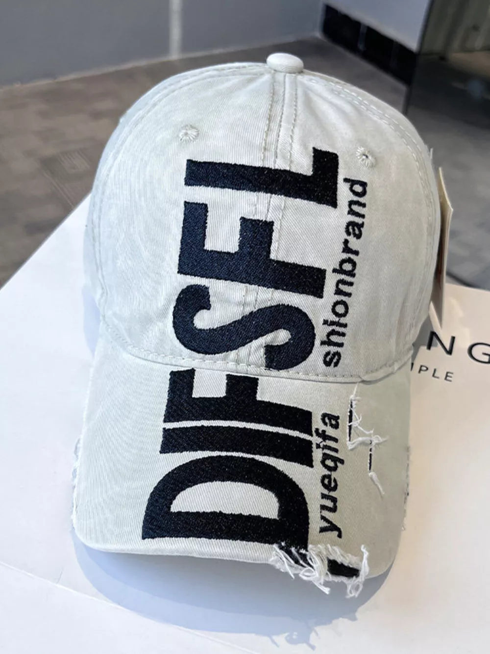 Beige distressed baseball cap with black text and frayed brim.
