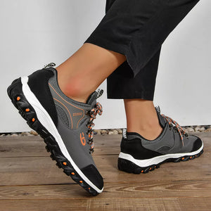 Grey and black lace-up low-top sneakers with patterned orange laces and white soles.