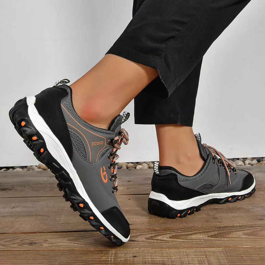 Grey and black lace-up low-top sneakers with patterned orange laces and white soles.
