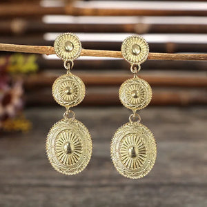 Gold sunburst drop earrings with intricate embossed details and oval pendants.