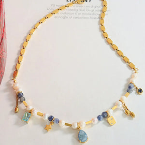 Gold celestial charm necklace with pearls, blue beads, and star, gem, and charm pendants.